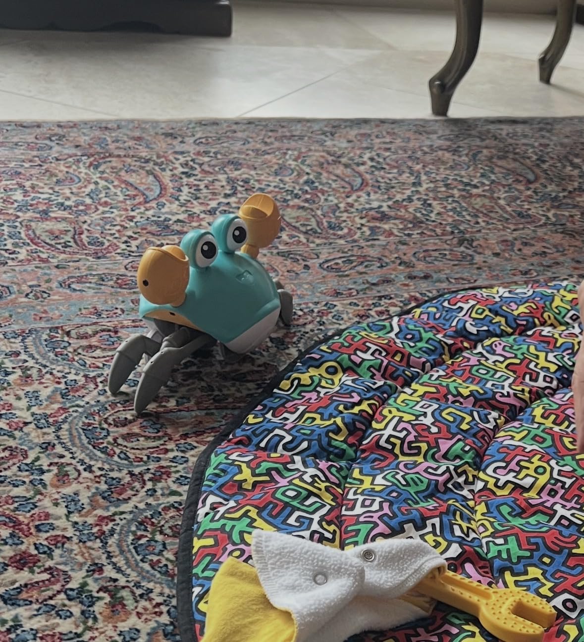 Green Crawling Crab toy walking across a patterned rug toward a baby play mat