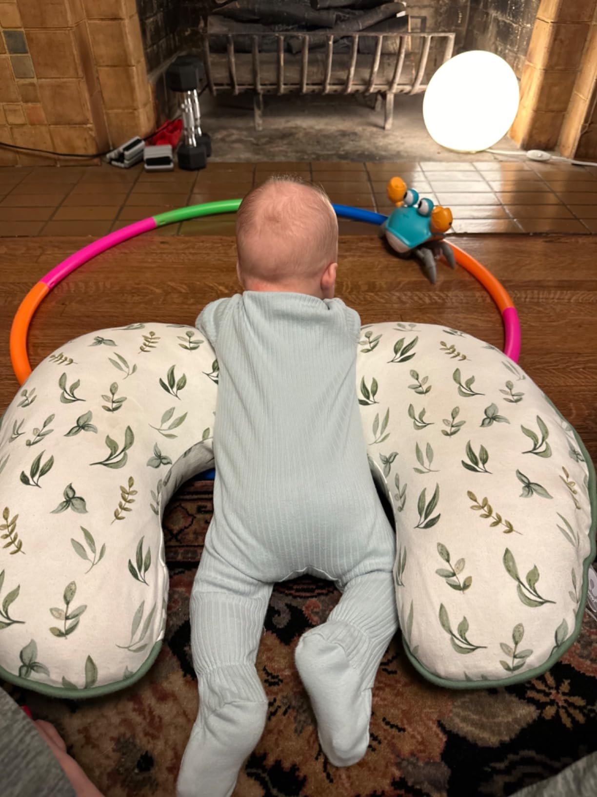 Baby on a nursing pillow during tummy time, watching a crawling crab toy on the floor