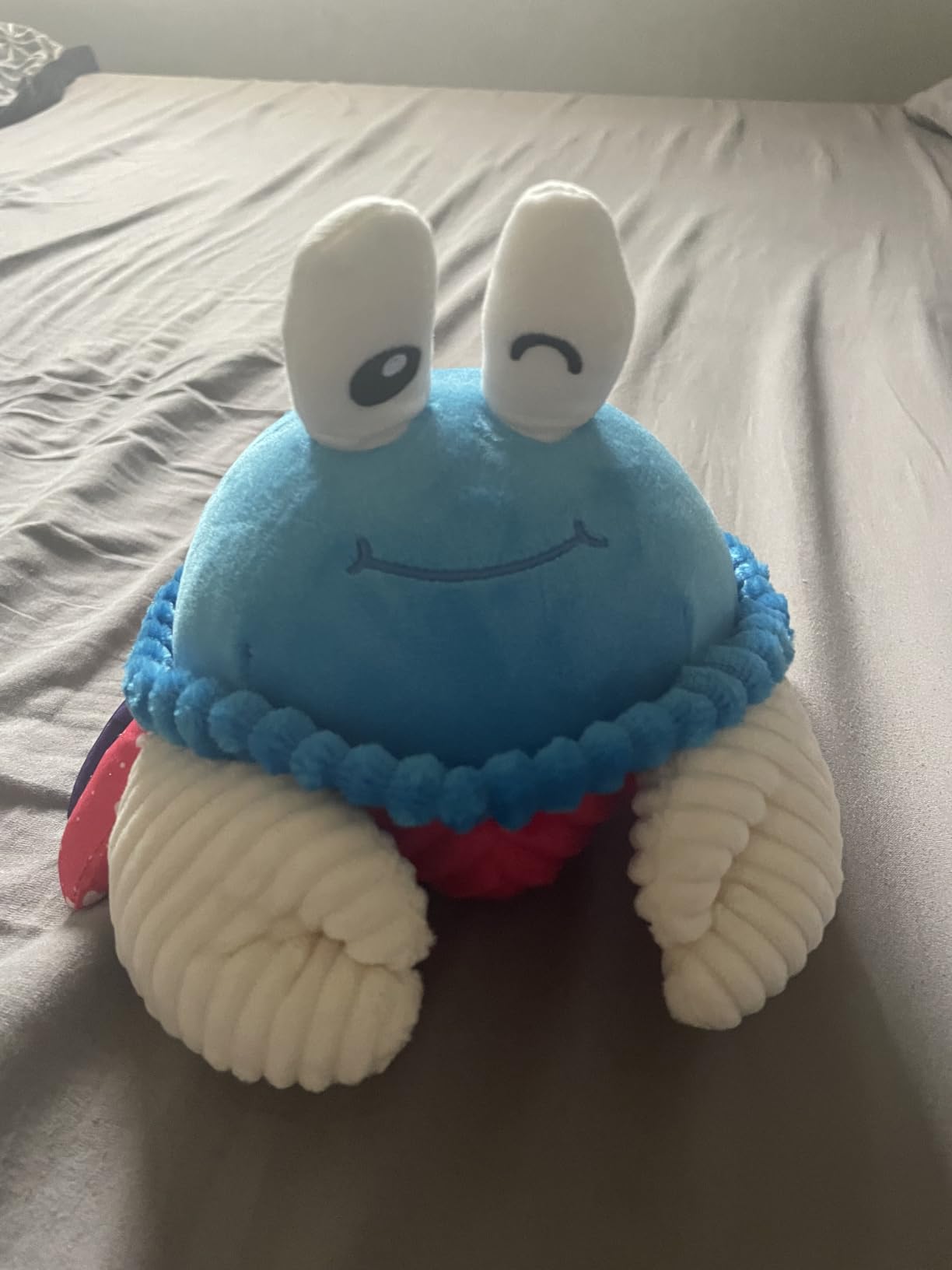 Blue plush musical crab toy with a winking face sitting on a bed