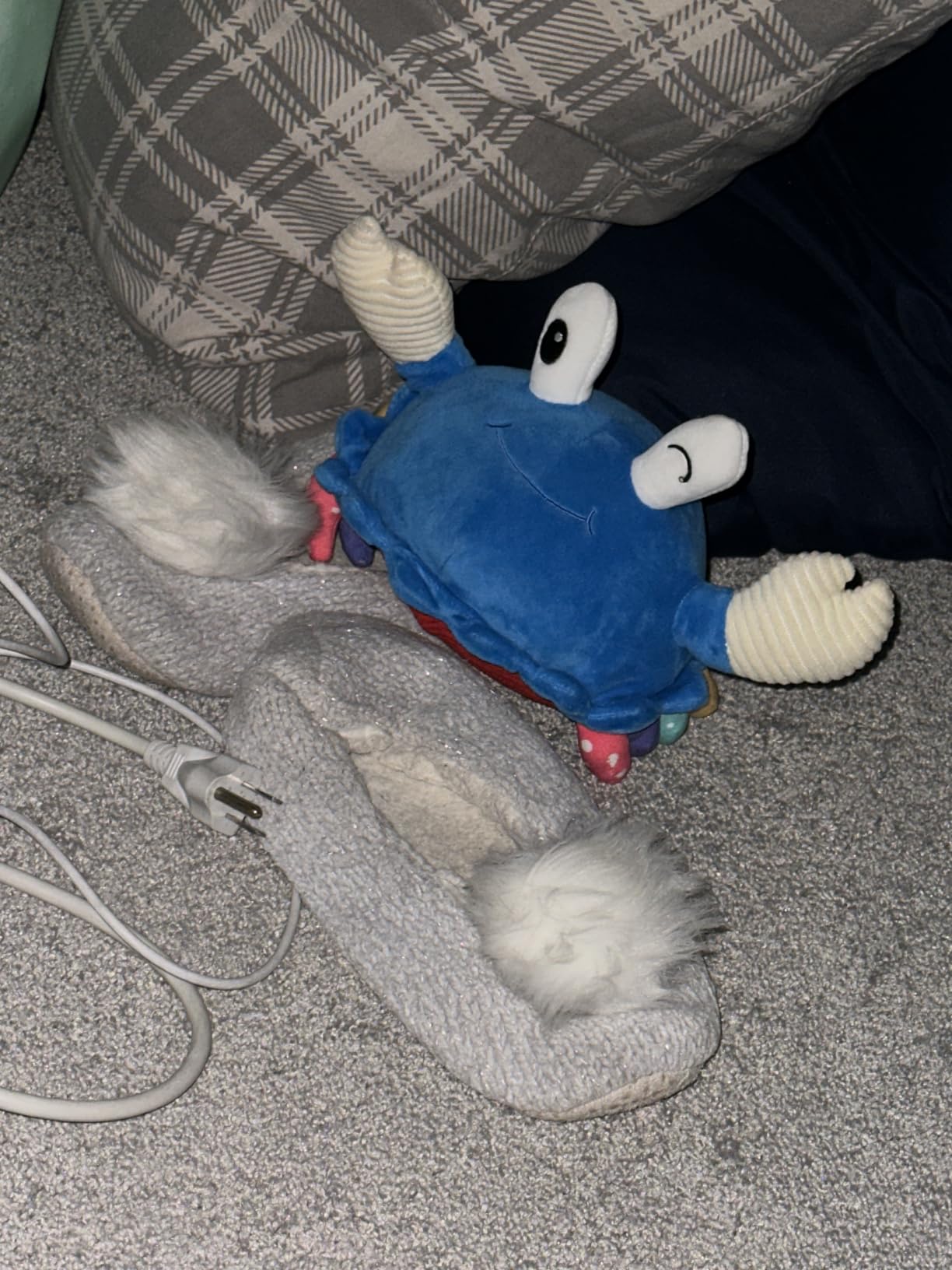 Blue plush crab toy on the carpet next to slippers and a charging cable